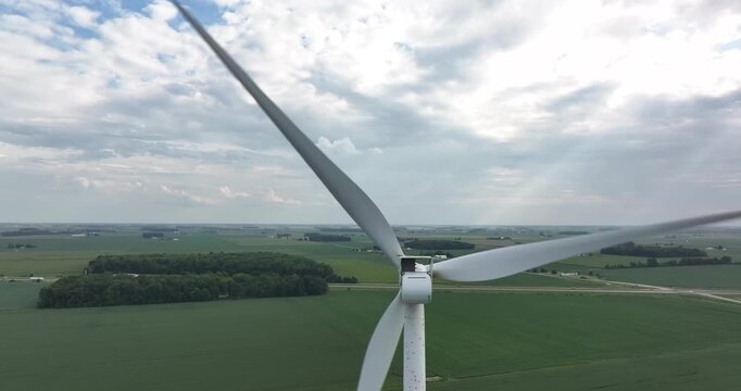 Aerial view of a towering wind turbine standing tall over vibrant green fields under a cloudy sky, Monroeville, Indiana, United States.