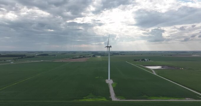 Aerial view of wind turbine standing tall amidst verdant fields, its blades reaching towards a sky full of clouds, Monroeville, Indiana, United States.