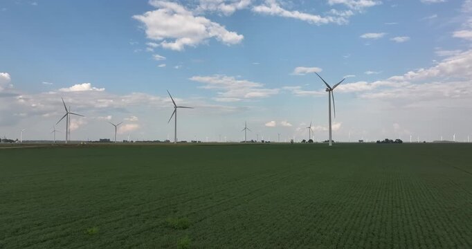 Aerial view of many wind turbines in a green field under a vast cloudy sky, a rural landscape of renewable energy, Monroeville, Indiana, United States.
