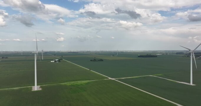 Aerial view of wind turbines puncturing the landscape, contrasting with the patchwork of green fields and white roads, Monroeville, Indiana, United States.