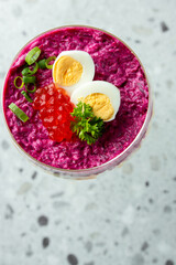 Layered vegetable salad in a glass, topped with boiled egg halves, red caviar, parsley, and green onions. Bright colors and elegant presentation