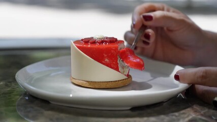 close-up of a white plate with a gourmet dessert in the centre, a woman's hand with red nail polish reaching out to take a spoonful