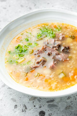 Top view of a bowl of clear broth soup with beef, carrots, celery, and parsley on a speckled gray countertop. Hearty homemade meal with visible ingredients