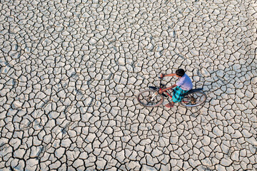 Chattogram, Bangladesh - 18 December 2019: Aerial view of a lone cyclist on a cracked, parched landscape, the stark white fissures contrasting with the figure.
