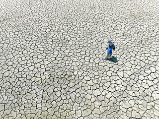 Chattogram, Bangladesh - 14 April 2023: Aerial view of a solitary figure with a blue umbrella traversing the parched, cracked earth, a stark testament to the relentless sun..