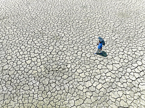 Chattogram, Bangladesh - 14 April 2023: Aerial view of a solitary figure with a blue umbrella traversing the parched, cracked earth, a stark testament to the relentless sun..