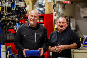 Two older aussie men working in parts section of mechanics workshop talking together