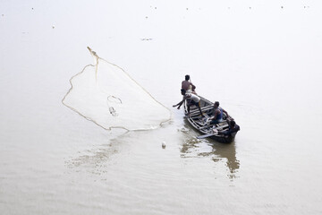 Muhuri, Bangladesh - 18 September 2024: Aerial view of fishermen casting their nets from a small boat, creating a stark contrast against the tranquil, shimmering water.