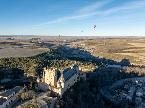 Segovia, Spain - 26 December 2023: Aerial view of the Alc&Atilde;&iexcl;zar castle standing proudly on a rocky crag, its beige stone contrasting against the deep green forest and the pale blue sky.