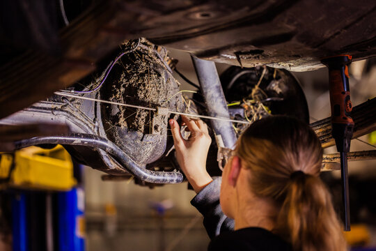 Female mechanic working on dirty car component underneath vehicle in workshop