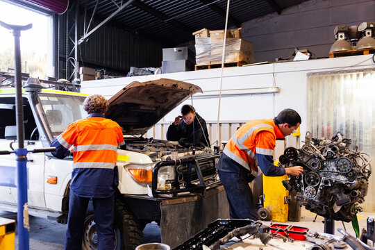 Mechanics diagnosing and repairing vehicle internal engine inside industrial workshop