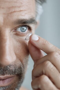 Mature caucasian male applying contact lens close-up. Contact Lens Safety Month