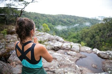 Woman standing on cliffs edge looking out at the rainforest view below