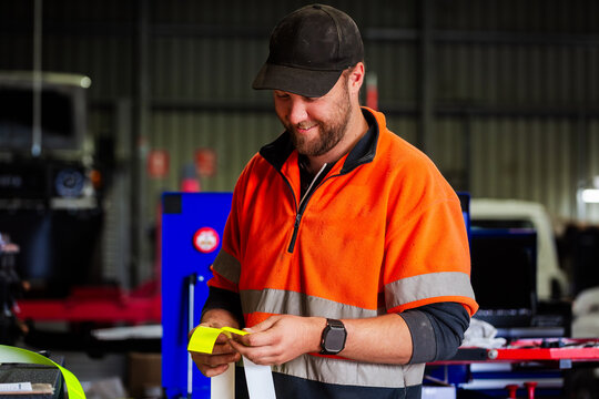 Workman cutting reflective tape for installation on mining fleet vehicle for safety in workshop
