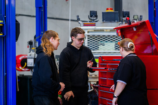 two mechanics in repair workshop chatting together with woman by toolbox cabinet