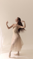 Fototapeta premium Graceful dancer in beige dress spraying perfume with flowing motion. Concept of beauty, perfume elegance, creative expression, femininity, health, wellbeing, and authentic lifestyle.