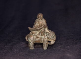 Fototapeta premium Antique Bronze Monk Riding Elephant with Scroll , Asian Spiritual Figurine with Patina