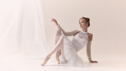 Graceful ballerina in white costume seated elegantly on pointe shoes. Concept of dance discipline, femininity, beauty, inner strength, luxury lifestyle, and artistic aesthetics. © master1305