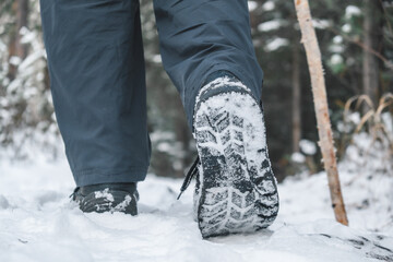 boots leave clear footprints in snow as traveler hikes through serene forest trail in winter. trees surround path, creating peaceful atmosphere. close up.