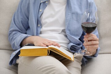 Obraz premium Woman with glass of wine reading book on sofa at home, closeup
