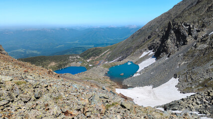 A stunning mountain landscape with two lakes, one deep blue and the other turquoise, surrounded by rocky terrain. Snow-capped peaks enhance the rugged beauty. The scene exudes grandeur and tranquility