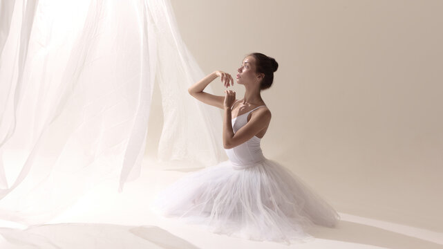 Ballet dancer in white tutu kneeling gracefully with serene upward gaze. Concept of mindfulness, feminine energy, inner calm, creative industries, rituals, and personal growth.