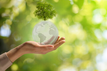Tree on Earth globe in woman's hand against blurred green background, closeup. Saving environment, care about planet
