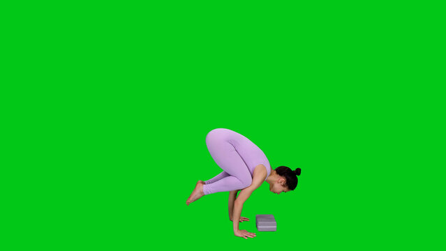 Young beautiful woman in bodysuit doing crow pose (bakasana) practicing yoga on green chroma key background