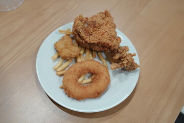 Fried chicken, french fries and fried shrimp donuts on white plates placed on a wooden table.