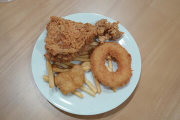 Fried chicken, french fries and fried shrimp donuts on white plates placed on a wooden table.