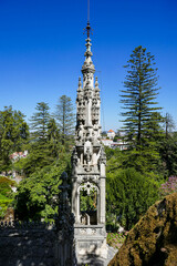 Obraz premium Decorative stone spire with intricate gothic carvings set against clear blue sky and green gardens, symbolizing European architecture, heritage, and historic monuments.