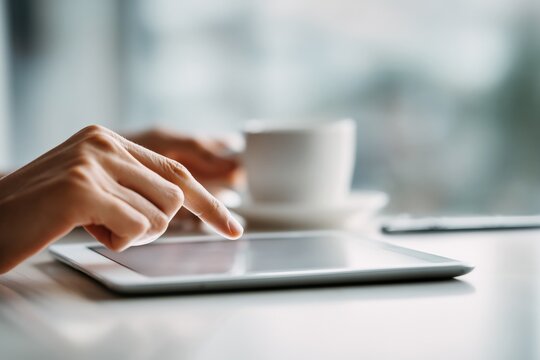 Close up hand using digital tablet on desk with coffee cup, modern technology and business concept