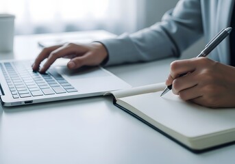 Person typing on a laptop and writing notes in a notebook at a desk