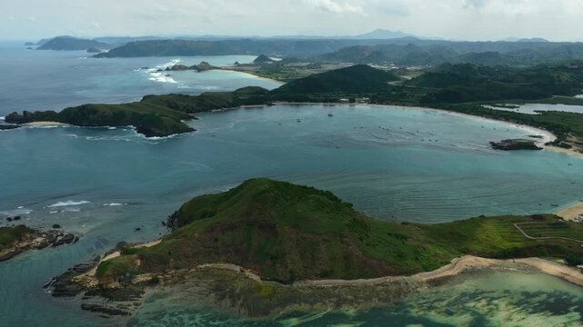 Drone drawback shot at Tanjung Aan headland in Lombok, revealing sweeping cliffs, turquoise ocean, and rugged coastline.