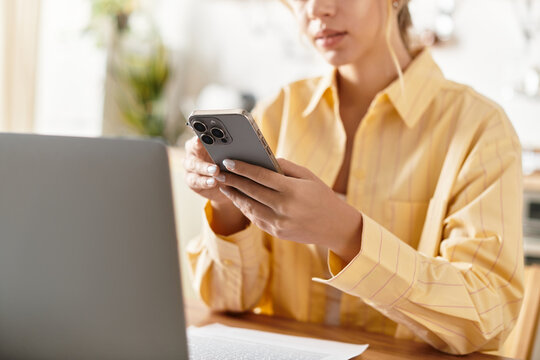 A woman checks her phone while sitting at a desk, enjoying a peaceful moment at home.