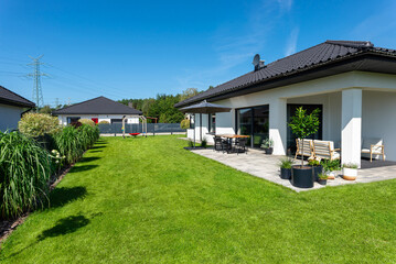 A beautiful garden with green grass, a patio table and umbrella visible, a house in beautiful summer weather, a very wide shot.