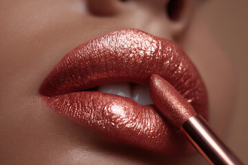 Close-up of applying shimmering lipstick for a captivating, glamorous look. The metallic shade enhances the lips with a radiant finish.