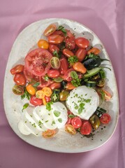 A vibrant antipasto is served on a platter, showcasing a medley of colorful heirloom tomatoes, peppery chillies, and fresh Mozzarella di Bufala Campana, garnished with aromatic basil and herbs