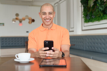 Bald Hispanic businessman having coffee break in cafe and using phone