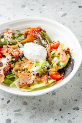 Fresh salad with mixed greens, cherry tomatoes, crispy bacon, chanterelles, sesame seeds, poached egg, and creamy dressing on speckled countertop