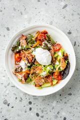 Fresh salad with mixed greens, cherry tomatoes, crispy bacon, chanterelles, sesame seeds, poached egg, and creamy dressing on speckled countertop