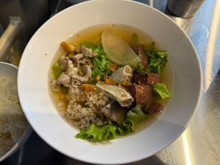 A bowl of Thai pork blood soup (Tom Luead Moo) with minced pork, pork liver, pork blood cubes, intestines, radish, and fresh lettuce