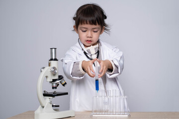 A young child in a lab coat conducts an experiment using a pipette and test tubes beside a microscope, showcasing a budding interest in science.