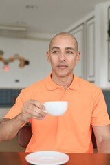 Man holding coffee cup inside cafe restaurant wearing orange polo shirt