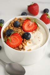 Tasty yogurt with granola, berries and spoon on white table, closeup