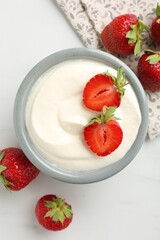 Delicious yogurt in bowl and strawberries on white marble table, flat lay