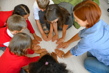School kids and teacher sitting in circle on floor, connecting their hands. Morning Circle.