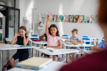 School children sitting at the desk in classroom on the lesson, raising hands.