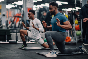 Obraz na płótnie Canvas Two young men doing lunges and stretching in the gym