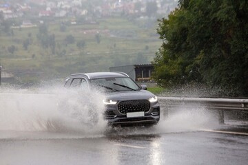 A car drives on a road flooded by rain. Heavy rainfall, climate change.